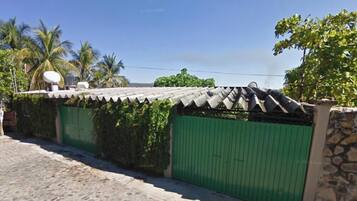A gated property with a tiled roof and a green gate, surrounded by greenery and palm trees.