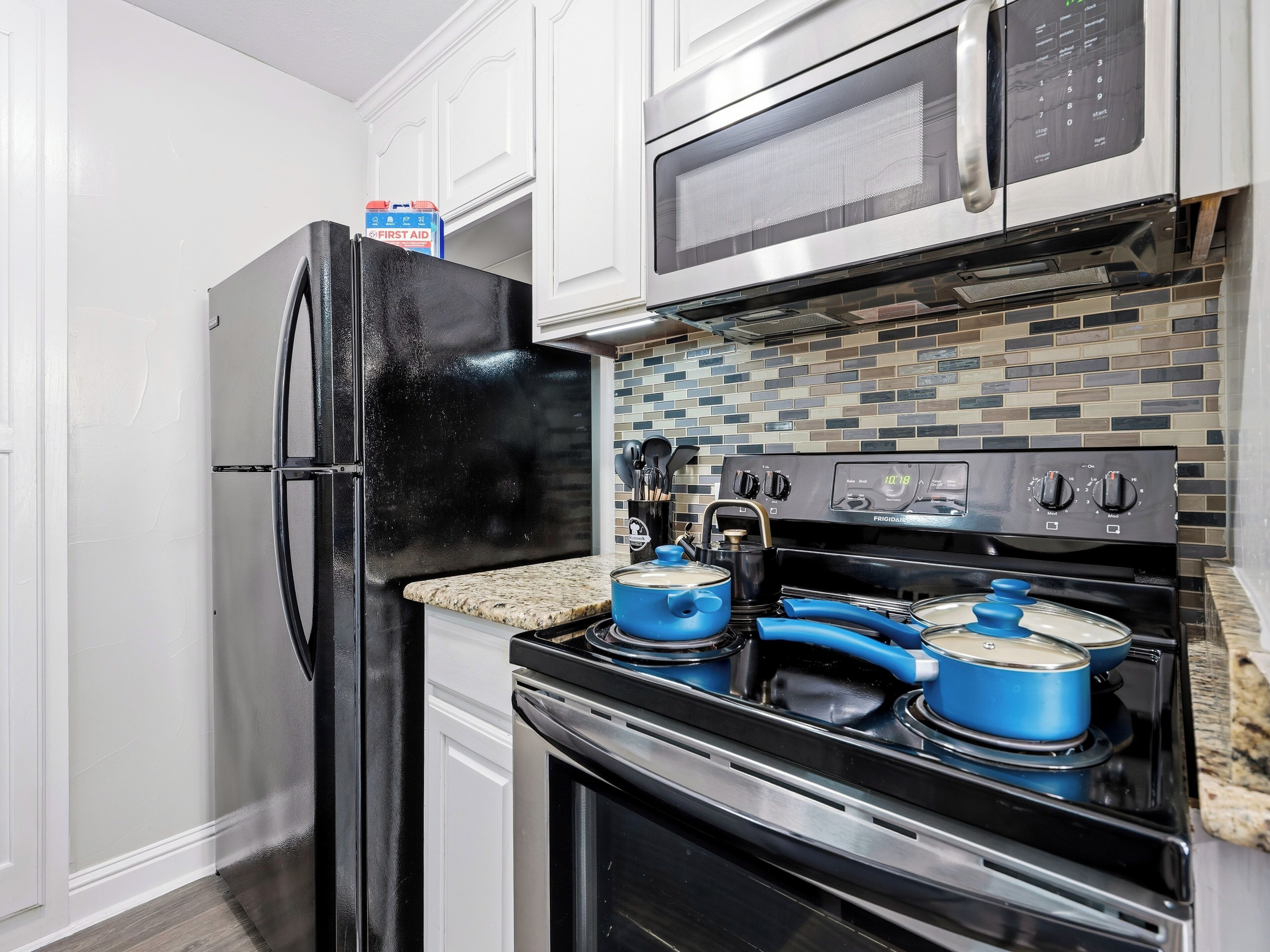 A kitchen with a black refrigerator, a microwave, a stove with blue pots, and a tiled backsplash.