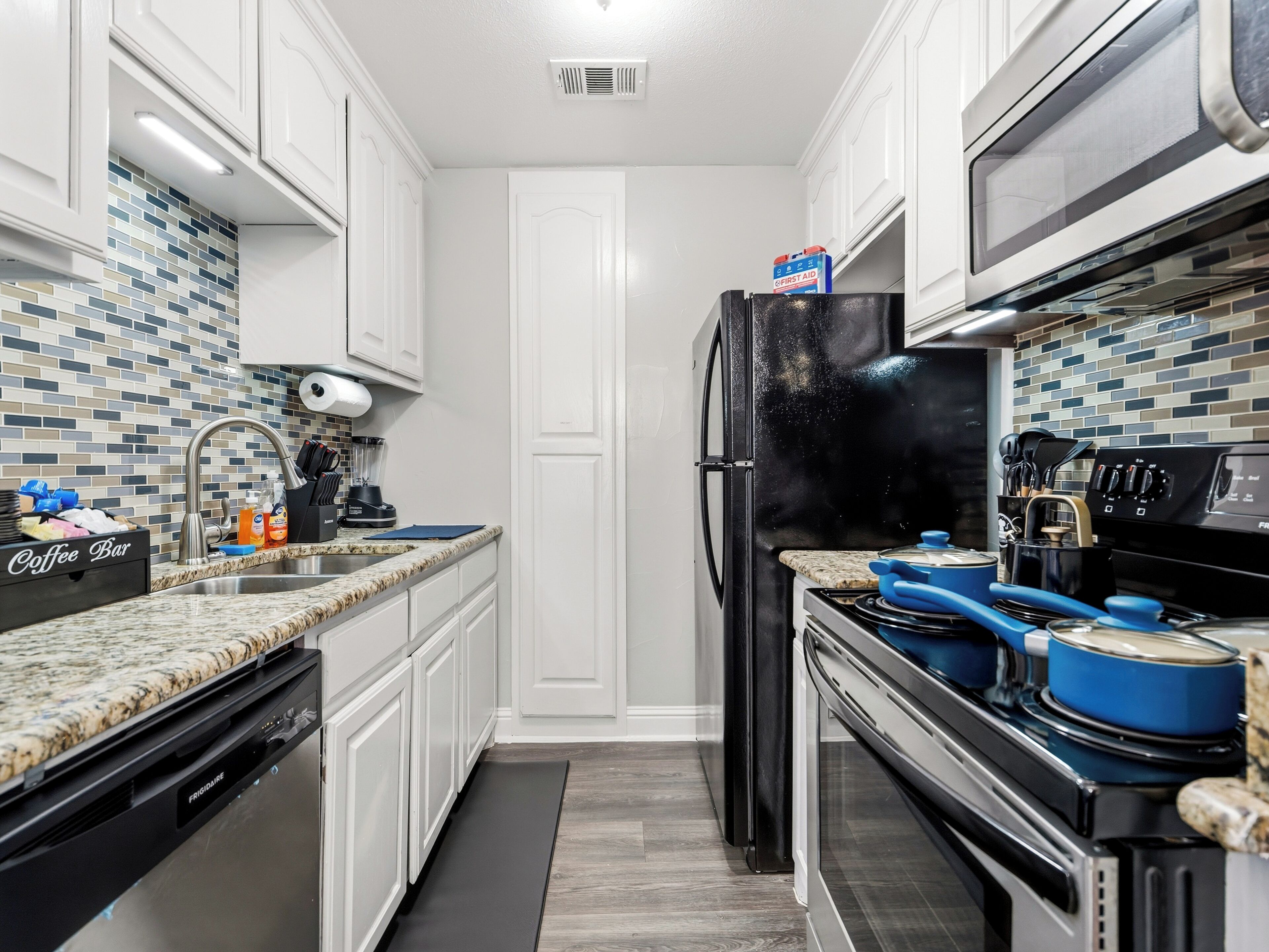 Una cocina con armarios blancos, un refrigerador negro, una estufa y un microondas.