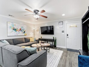 A modern living room with a grey sofa, a coffee table, a TV, and a ceiling fan. - Cozy Comfort! Walking Distance to Entertainment! (Arlington)