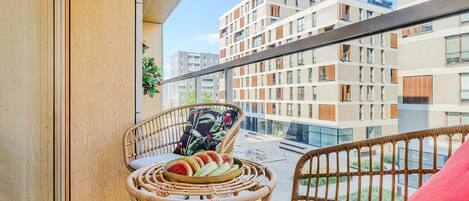 Un balcon agrémenté de meubles en osier, d’une table et d’un saladier rempli de fruits.