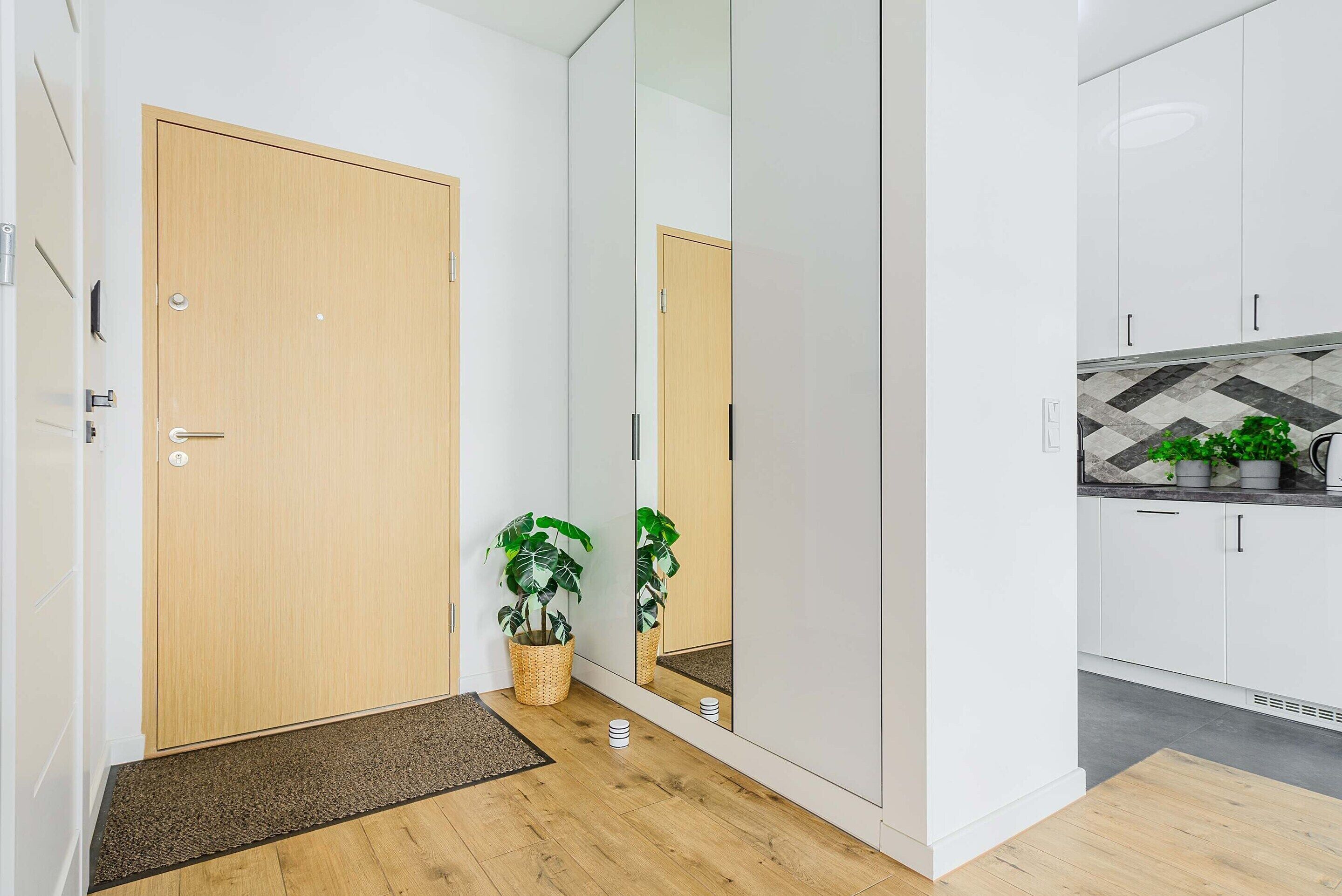 Ein modernes Interieur mit Holztür, großem Spiegel und Küchenbereich mit Schränken und Arbeitsplatte.