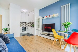 A modern living room with a flat-screen TV, a sofa, and a dining area with colorful chairs. - Stay Near Railway Hub (Warsaw)