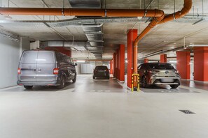 A parking garage with multiple levels, concrete pillars, and overhead pipes. - Stay Near Railway Hub (Warsaw)