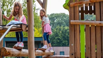 Two children playing on a wooden play structure with a slide and climbing elements.