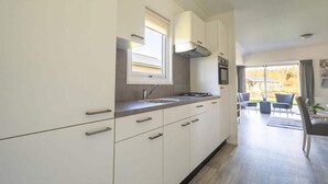 A modern kitchen with white cabinetry, a window above the sink, and a view of the outdoor patio area. - Charming Chalet Near Efteling (Kaatsheuvel)