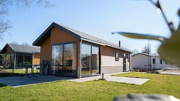 A modern two-story house with a large glass door entrance, a patio with outdoor furniture, and a well-maintained lawn.