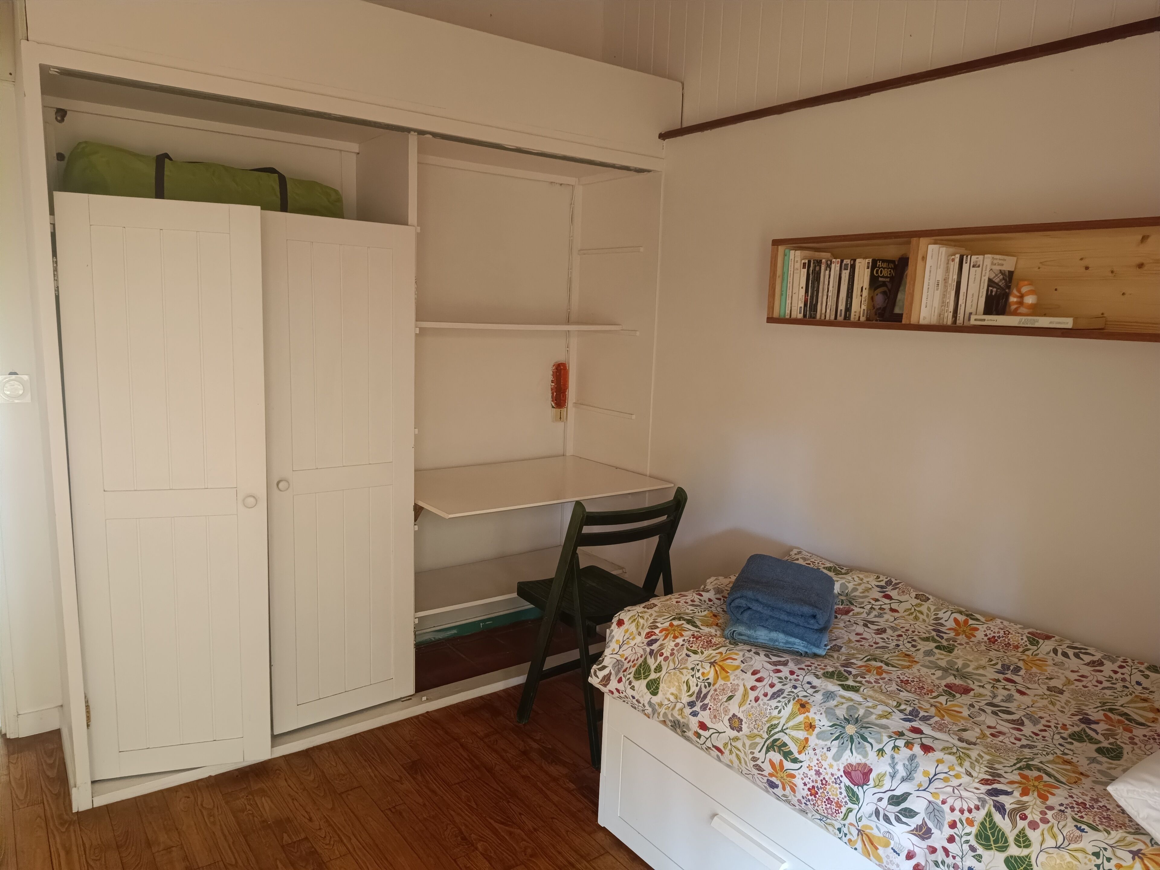 Een slaapkamer met een bed, een stoel, een bureau en een kledingkast.