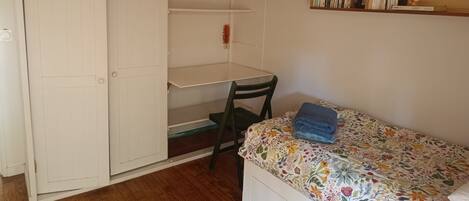 Een slaapkamer met een bed, een stoel, een bureau en een kledingkast.