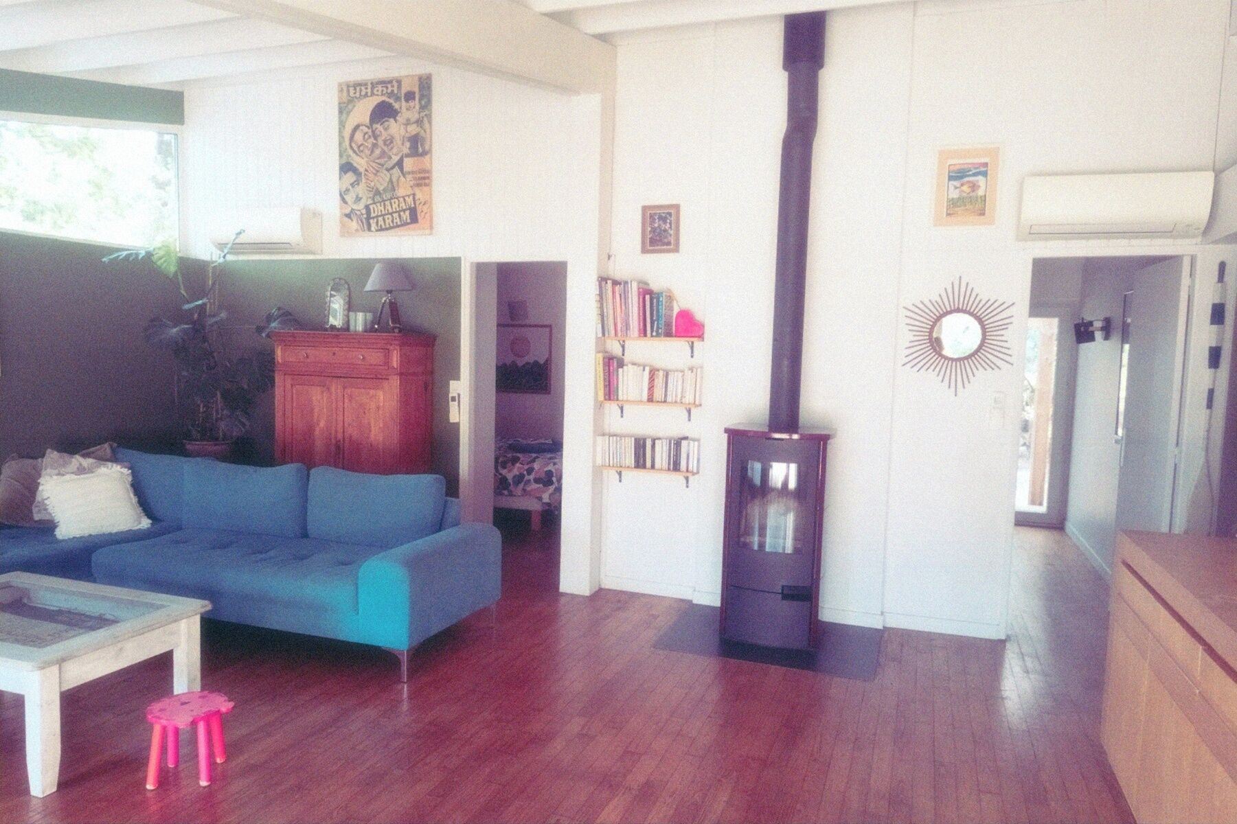 Una sala de estar con un sofá azul, una mesita, un taburete rosa, una estantería y una chimenea.