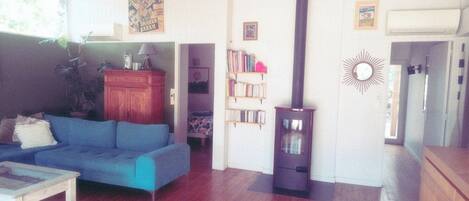 Una sala de estar con un sofá azul, una mesita, un taburete rosa, una estantería y una chimenea.