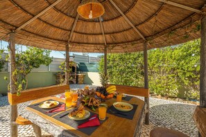 An outdoor dining area with a thatched roof, a brick oven, and a variety of food and drinks. - Peaceful retreat w/ heatable pool & garden (Carvoeiro)