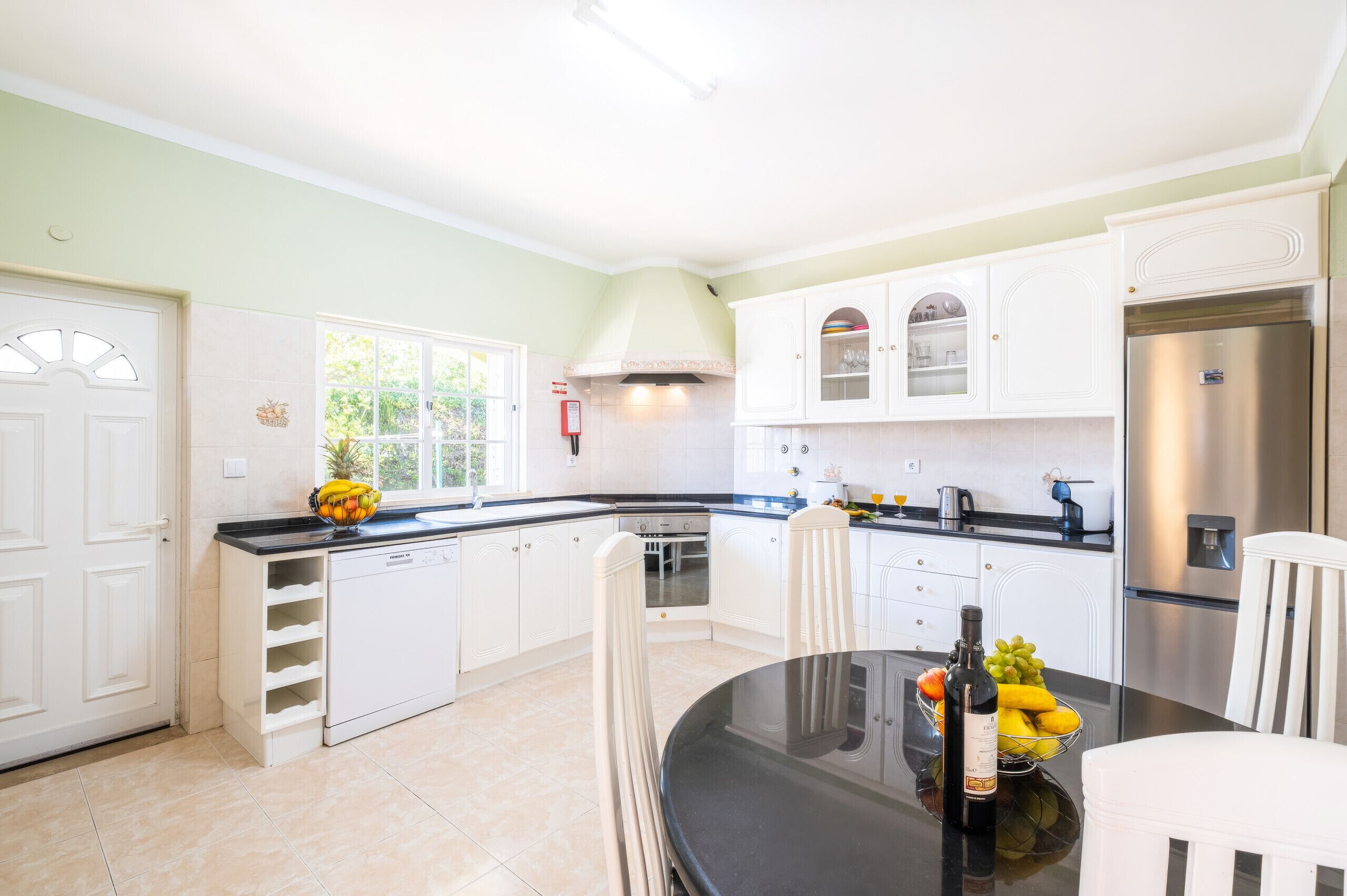 A modern kitchen with white cabinetry, a stainless steel refrigerator, and a dining area with a glass table.