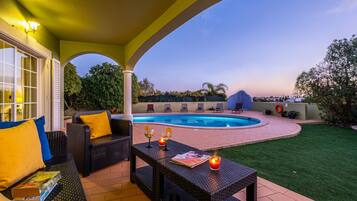 A covered outdoor area with a pool, seating, and a view of the surrounding landscape.