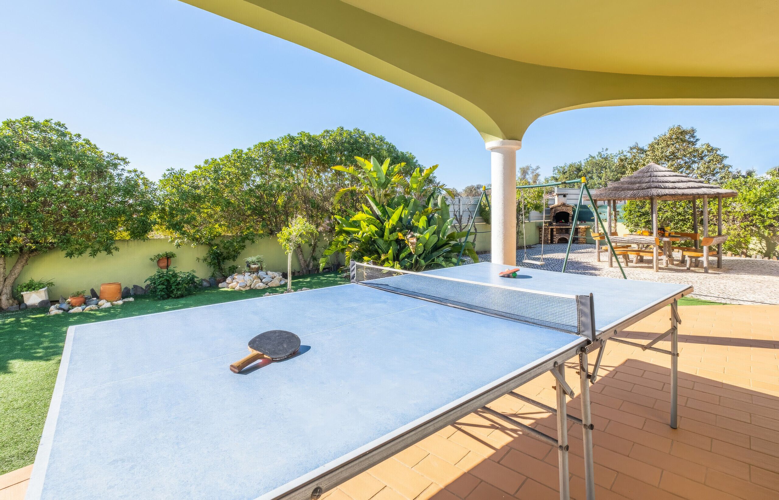 An outdoor ping pong table with a net, a thatched-roof gazebo, and a brick patio.