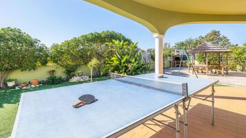 An outdoor ping pong table with a net, a thatched-roof gazebo, and a brick patio.