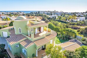 A multi-story house with a curved balcony, surrounded by greenery and a coastal view. - Peaceful retreat w/ heatable pool & garden (Carvoeiro)