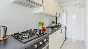 Uma cozinha moderna com armários brancos, fogão de aço inoxidável e bancada preta.