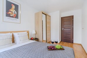A hotel room with a bed, a painting of a woman, a wooden wardrobe, and a tray of grapes and wine glasses. - Apartment With Private Balcony (Warsaw)