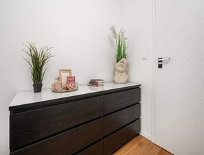 Une salle de bain moderne avec un mur recouvert de carreaux blancs, un meuble-lavabo en bois foncé doté d’un miroir et une plante en pot.