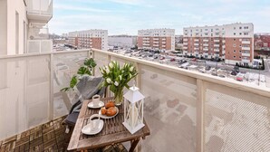 A balcony with a table set for two, a vase with flowers, and a view of apartment buildings. - Beautiful Seaview Flat in Stagadon Island (Łódź)
