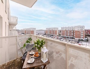 Ein Balkon mit Tisch für zwei Personen, einem Blumenvasen und Blick auf Wohnhäuser.