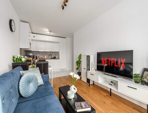 A modern living room with a sofa, a coffee table with a book, a TV displaying 'NETFLIX', and a kitchen in the background. - Beautiful Lodz Apartment for 6 Guests (Łódź)