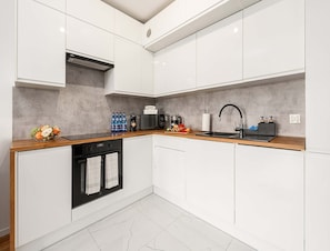 A modern kitchen with white cabinetry, a black stove, and a wooden countertop. - Beautiful Lodz Apartment for 6 Guests (Łódź)