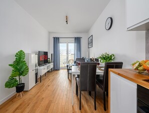 Eine moderne Wohnung mit Essbereich, einem Wohnzimmer mit Fernseher und einem Balkon mit Vorhängen.