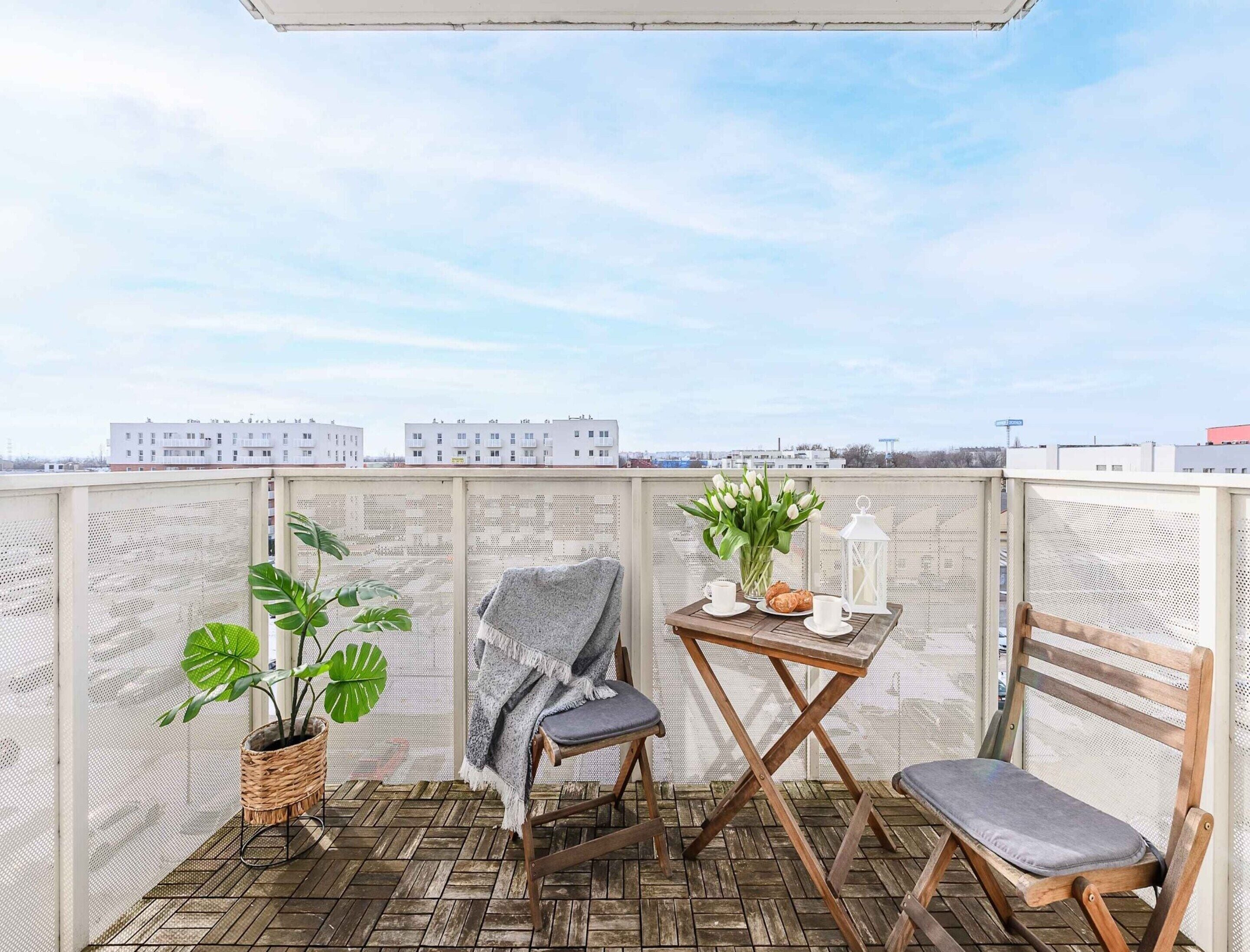 A balcony with a wooden floor, a chair, a table with a vase of flowers, and a potted plant.