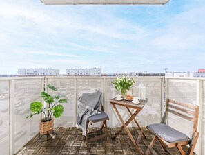 A balcony with a wooden floor, a chair, a table with a vase of flowers, and a potted plant. - Beautiful Lodz Apartment for 6 Guests (Łódź)