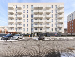 Un immeuble résidentiel à plusieurs étages, doté de balcons, d’un espace de stationnement dallé et surplombant un ciel dégagé.