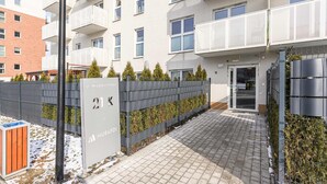 A modern apartment building entrance with a paved walkway, a metal fence, and a sign indicating the address. - Beautiful Seaview Flat in Stagadon Island (Łódź)