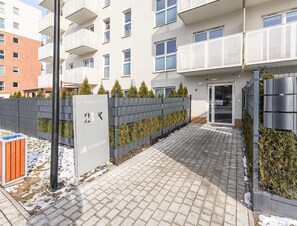Ein moderner Hauseingang eines Mehrfamilienhauses mit einem gepflasterten Weg, einem Metallzaun und einem Schild mit der Hausnummer.