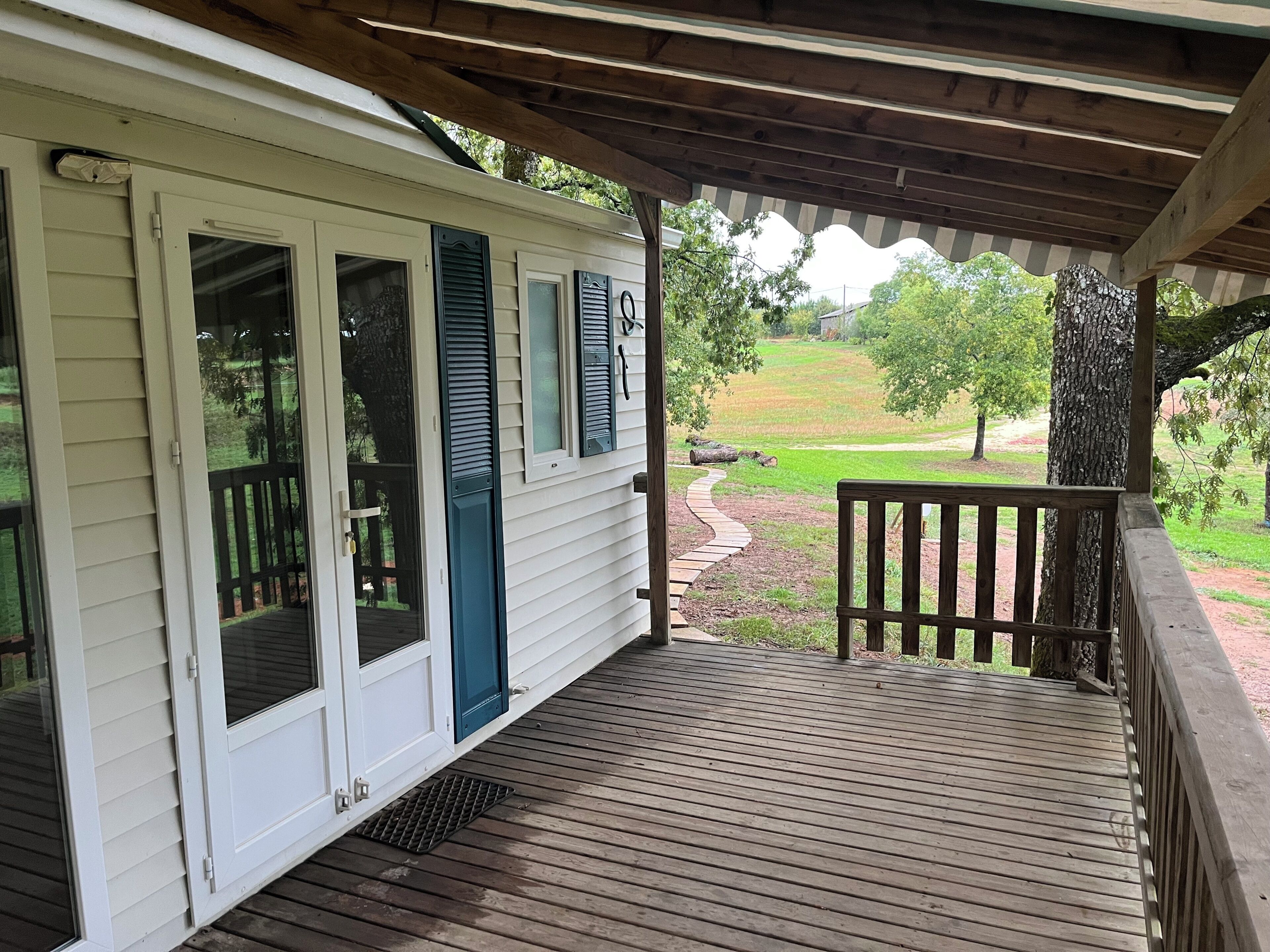 A covered porch with a wooden deck, a view of a grassy landscape, and a wooden railing.