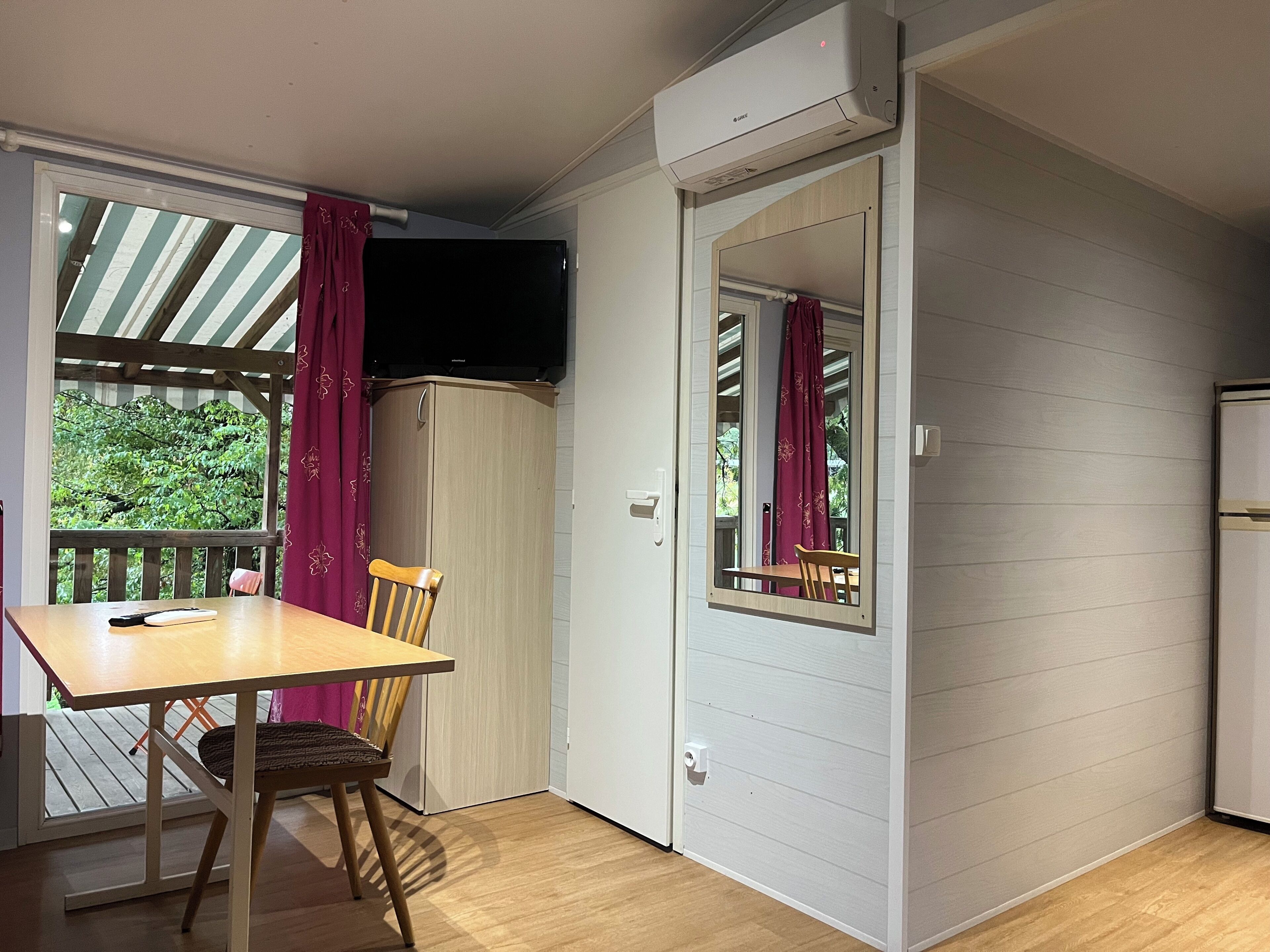 A room with a wooden table, a chair, a television, and a door leading to a balcony.