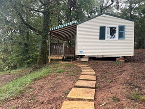 A small cabin with a porch and a stone pathway leading to it, surrounded by trees. - A quiet mobile home surrounded by nature (Gavaudun)