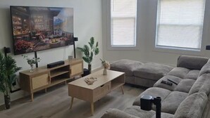 A living room with a sectional sofa, a coffee table, a TV, and a large window. - Spacious 5-bedroom house in awesome Detroit with AC (Detroit)