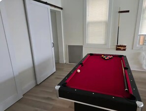 A pool table with balls, a door, and a window with blinds.