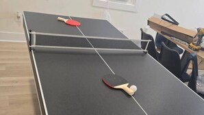 A ping pong table with two paddles and a ball, a window with blinds, and a wooden floor. - Spacious 5-bedroom house in awesome Detroit with AC (Detroit)