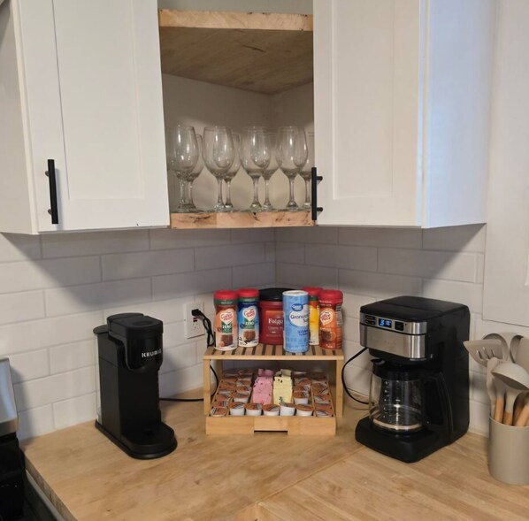 A kitchen with a coffee maker, a spice rack, and a cabinet with wine glasses.