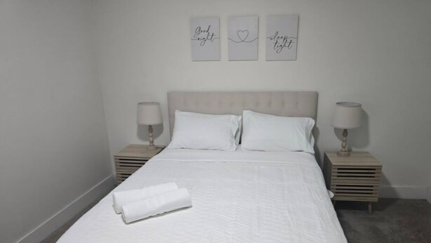 A neatly made bed with a quilted cover, two bedside tables with lamps, and three wall art pieces above the bed. - Spacious 5-bedroom house in awesome Detroit with AC (Detroit)