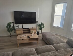 A living room with a large flat-screen TV, a wooden coffee table, a sofa, and two potted plants.