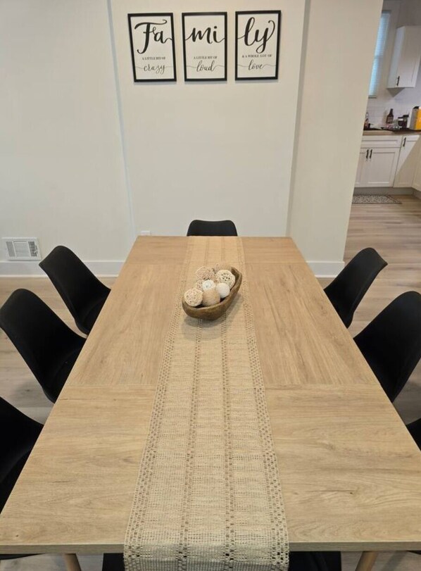 A dining area with a wooden table, black chairs, and a woven placemat. Three framed inspirational quotes hang on the wall above the table.