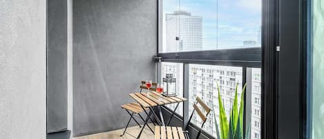 Un balcón con mesa y sillas de madera, una planta en maceta y vistas de la ciudad.