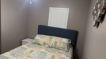 Une chambre à coucher avec un lit, une table de chevet, une fenêtre avec des stores et un ventilateur de plafond.