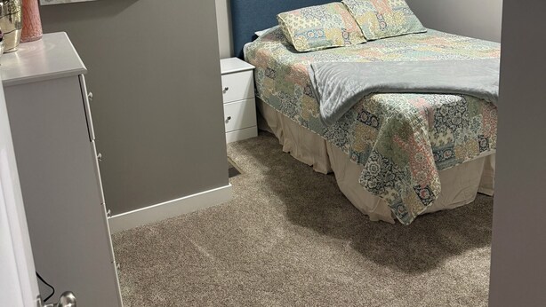 Een slaapkamer met een bed, nachtkastje, kaptafel, plafondventilator en een raam met jaloezieën.