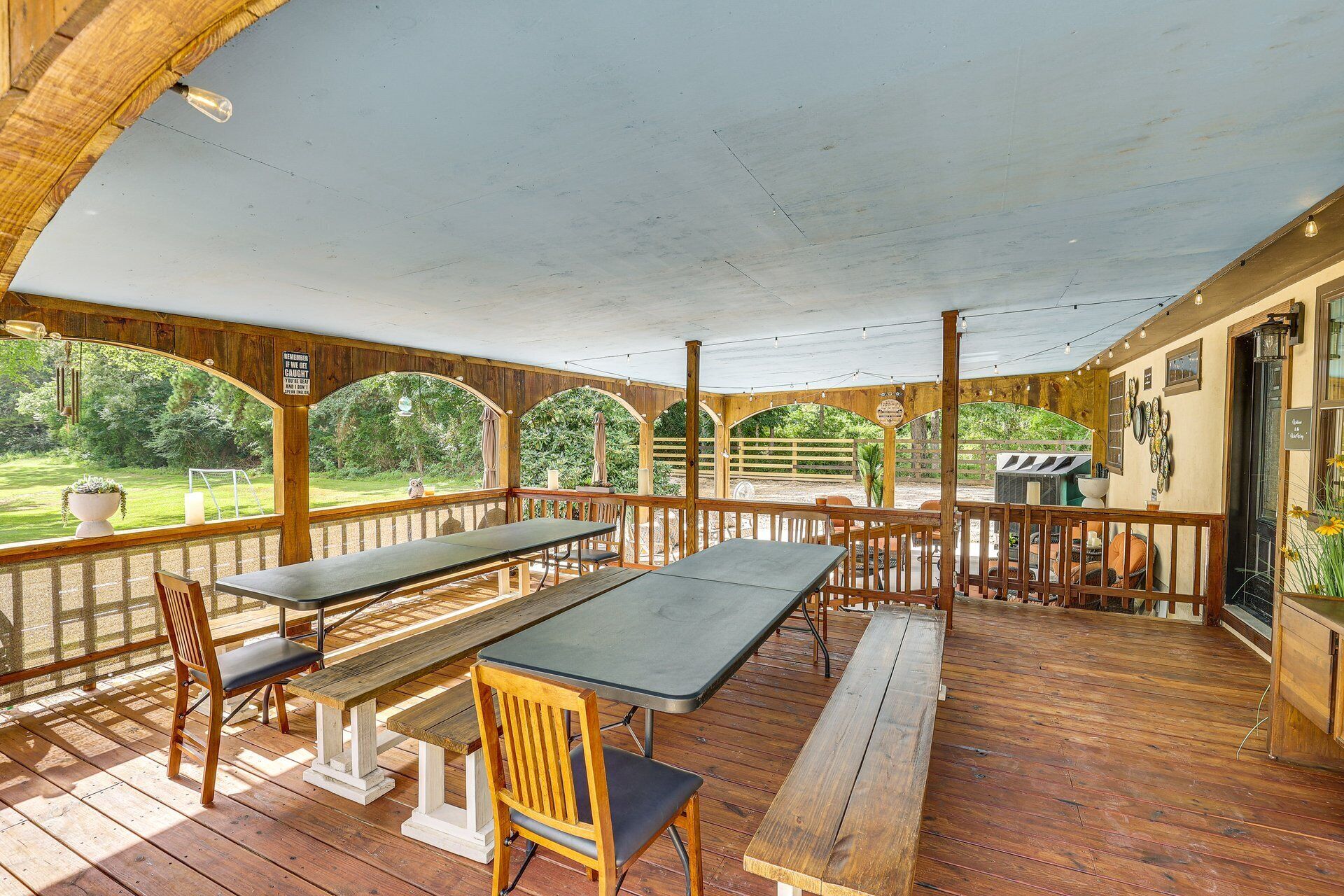 Une terrasse extérieure couverte, dotée de bancs et de tables en bois, d’un barbecue et offrant une vue sur la végétation environnante.