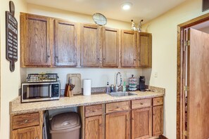 Una cocina con armarios de madera, microondas, lavabo y cubo de basura.