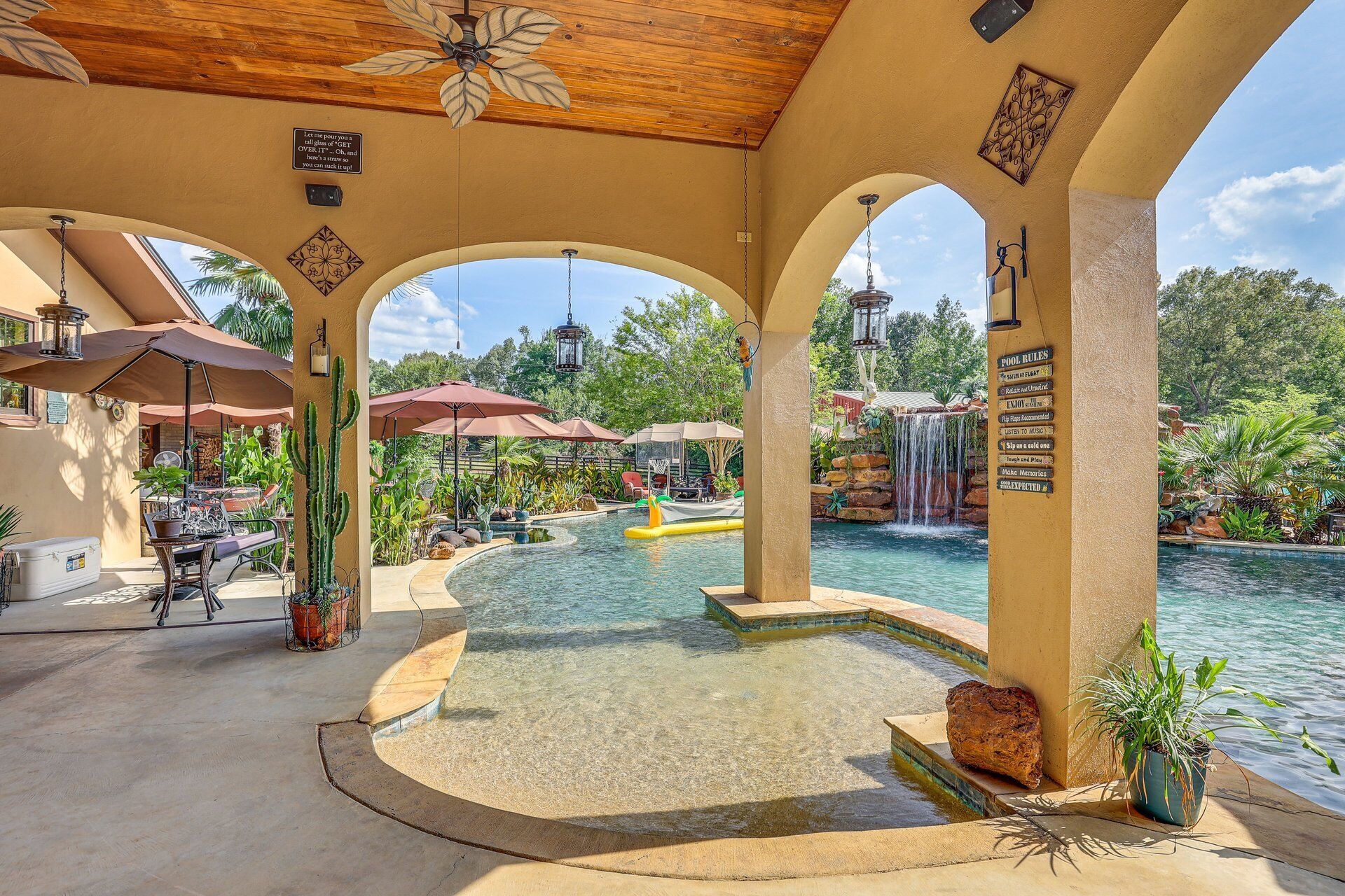 Un área de piscina con cascada, mobiliario exterior y un patio cubierto.
